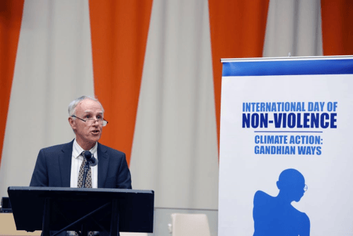 David Cortright speaking from a podium next to a banner reading "International Day of Nonviolence. Climate Action: Gandhian Ways."
